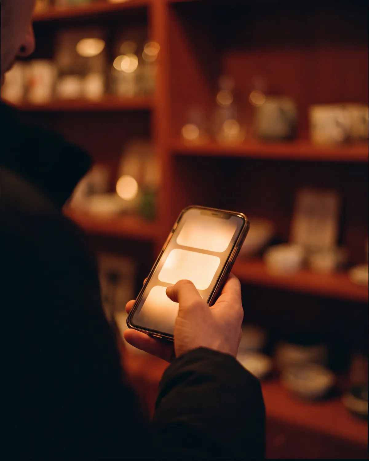 A hand holds a glowing phone in a dim shop, the screen light falling on the fingers.